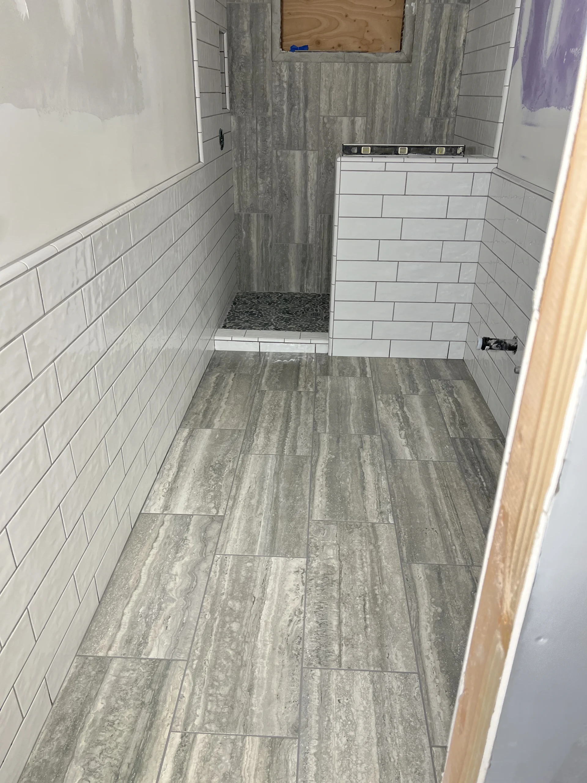Modern bathroom with gray and white tile walls and floor, featuring a tiled shower enclosure.
