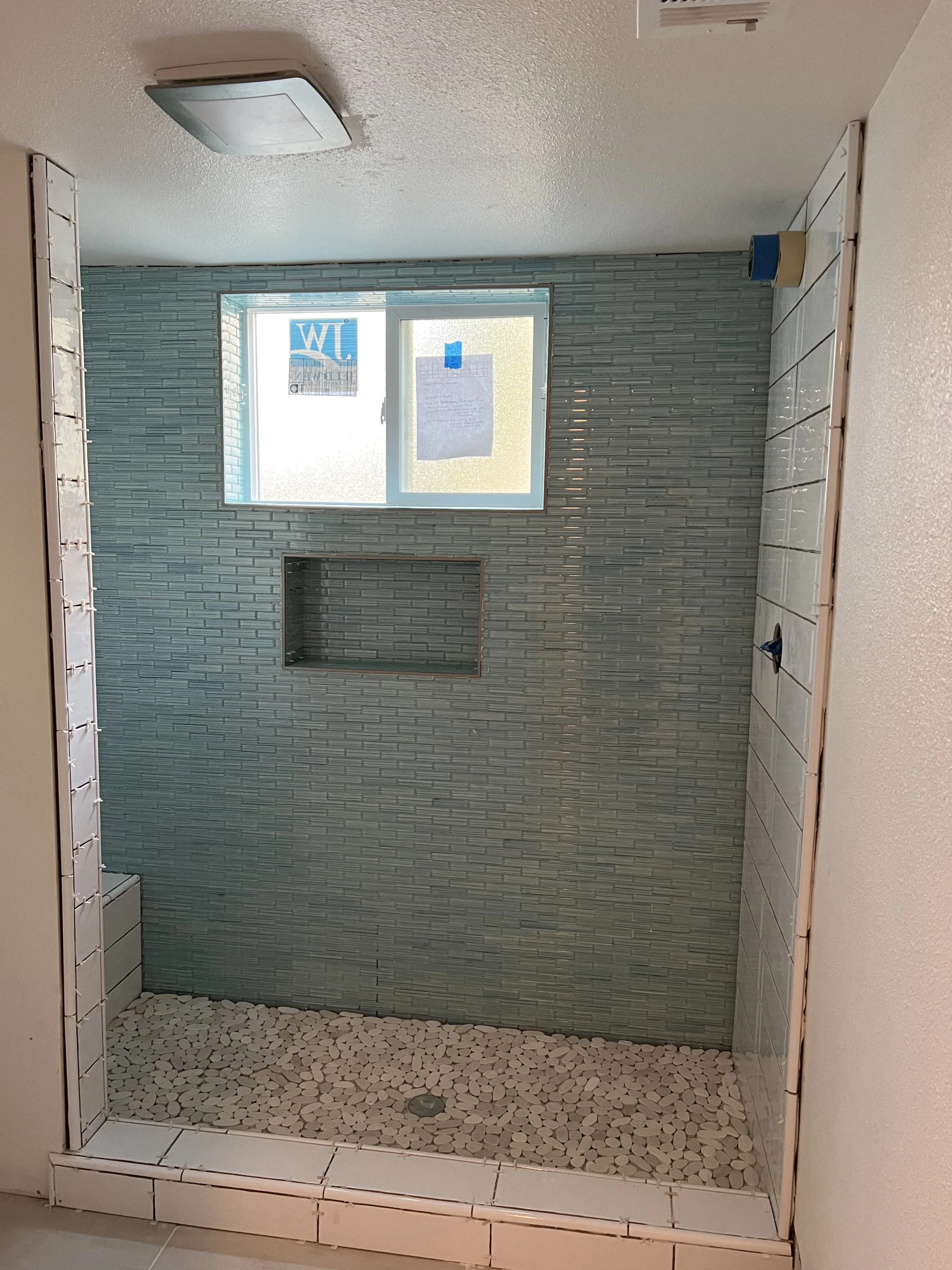 Walk-in shower with light blue horizontal tile and white pebble floor in Fresno bathroom renovation.